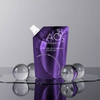 Purple stand-up pouch of Hydrate skincare product labeled A02 on a reflective surface, surrounded by clear glass spheres.