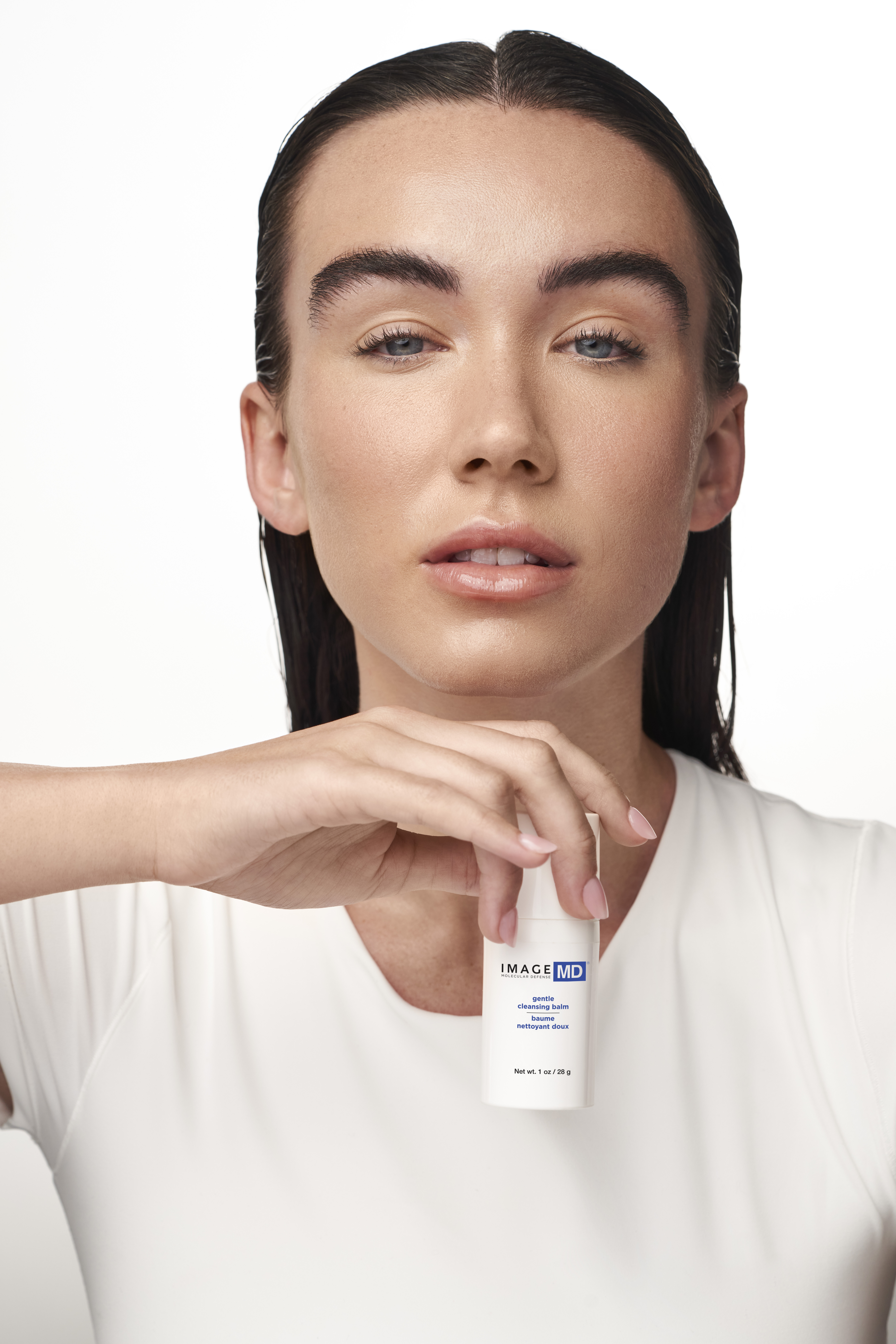 Close-up of a woman in a white top holding a white skincare bottle labeled IMAGE MD, focusing on the product near her chin.
