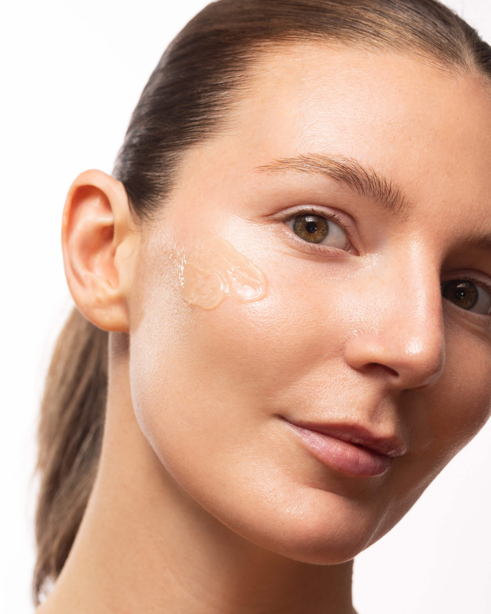 Close-up of a woman's right cheek, eye, and eyebrow against a white background, showing smooth skin and brown eye.